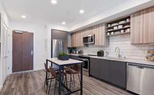 Redwood City Apartments - Kitchen With Beige And Grey Cabinets, White Countertops And Backsplash, Built-In Shelving, Stainless-Steel Appliances, And Dining Table With Chairs.