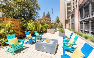 Apartments In Redwood City for Rent - Encore - Fire Pit With Wooden-Style Seating, Throw Pillows, And Landscaping.